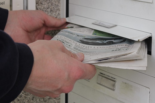 Die Zeitung wird von einem Zusteller oder Verteiler in einen Briefkasten gesteckt.